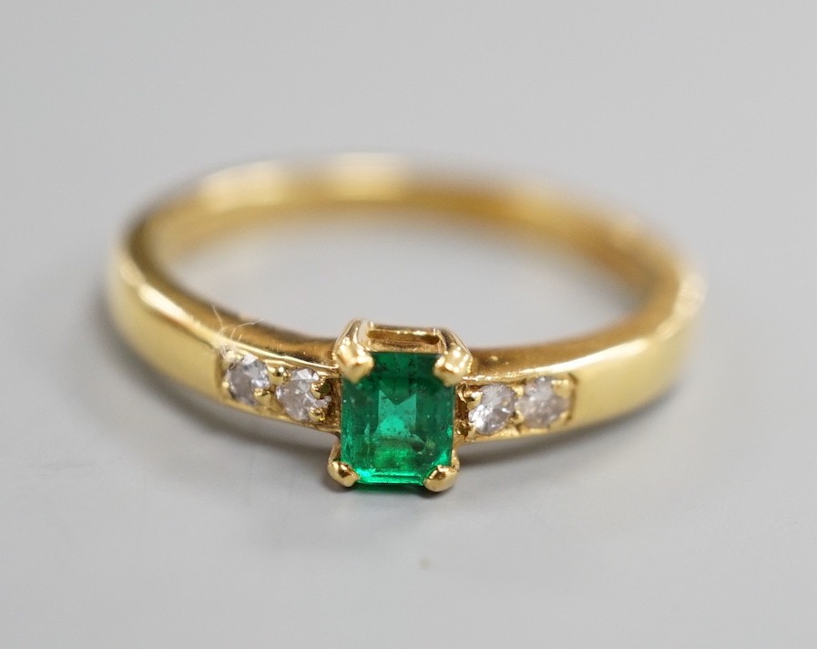 A modern 18ct gold and single stone emerald set ring, with four stone diamond set shoulders, size O, gross weight 3.4 grams